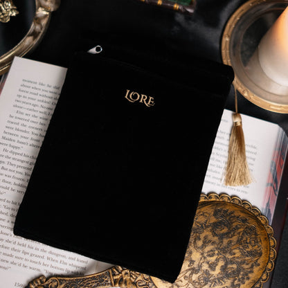 Black velvet pouch labeled 'LOVE' on an open book with a candle and decorative items.