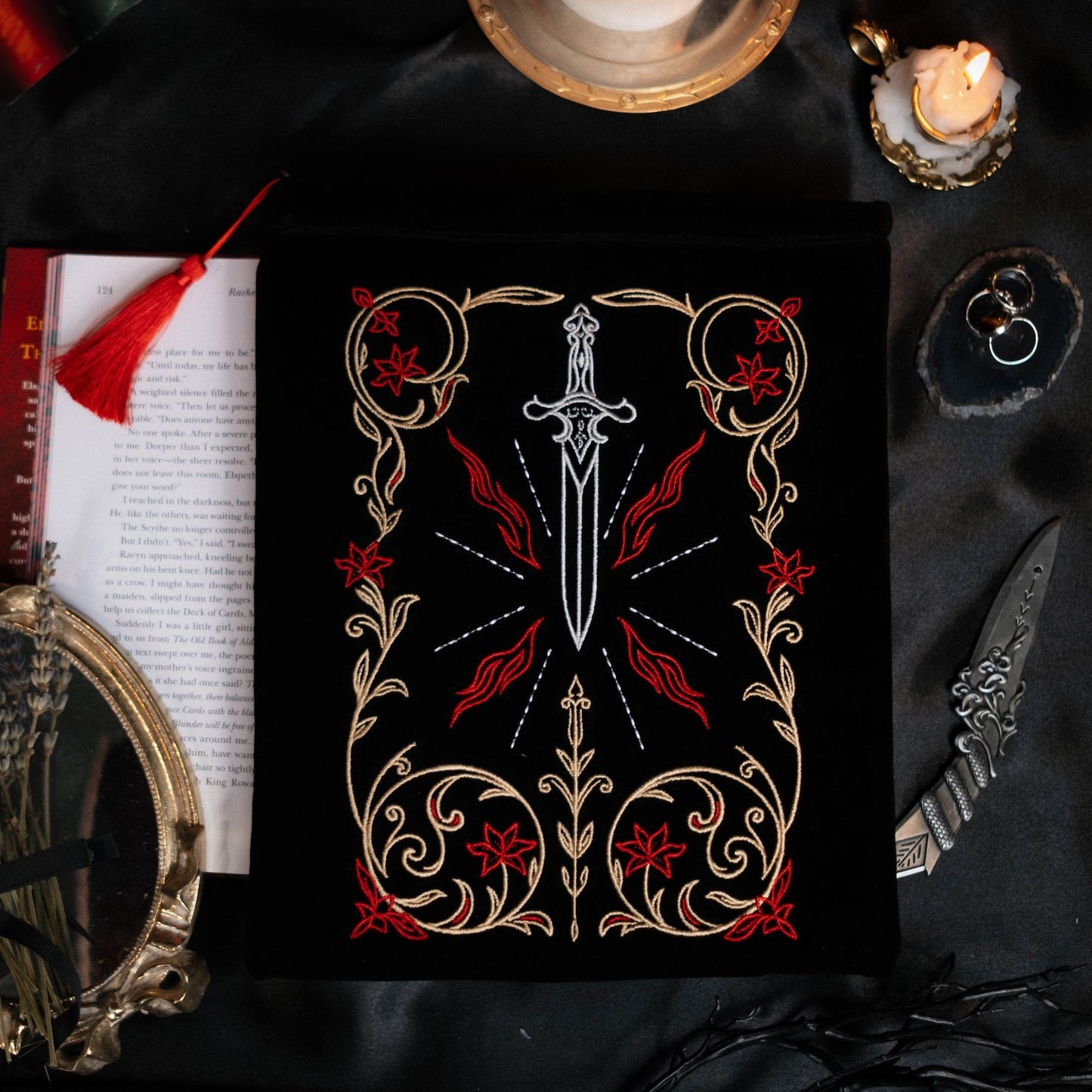 Decorative book sleeve with a sword design on a dark fabric background with candles and books.