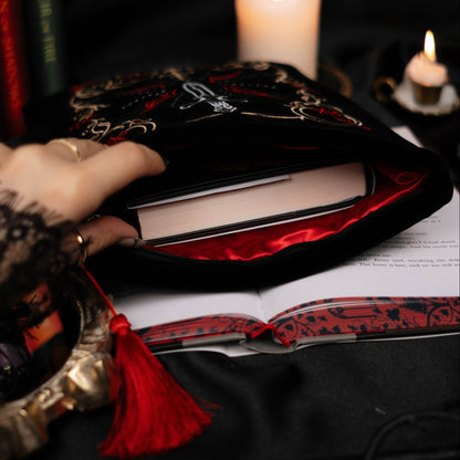 Close-up of a hand holding a red and black book sleeve open with candles and other items on a dark background