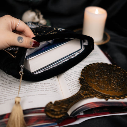 Hand holding open a book sleeve with a candle and mirror on a dark background