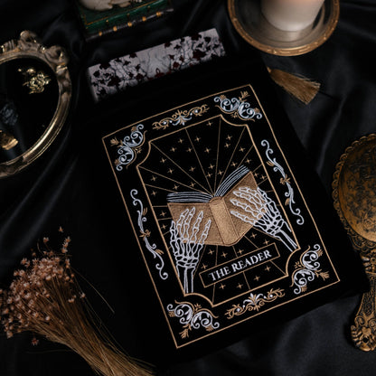 Book sleeve titled 'The Reader' with a candle and other mystical items on a dark fabric background