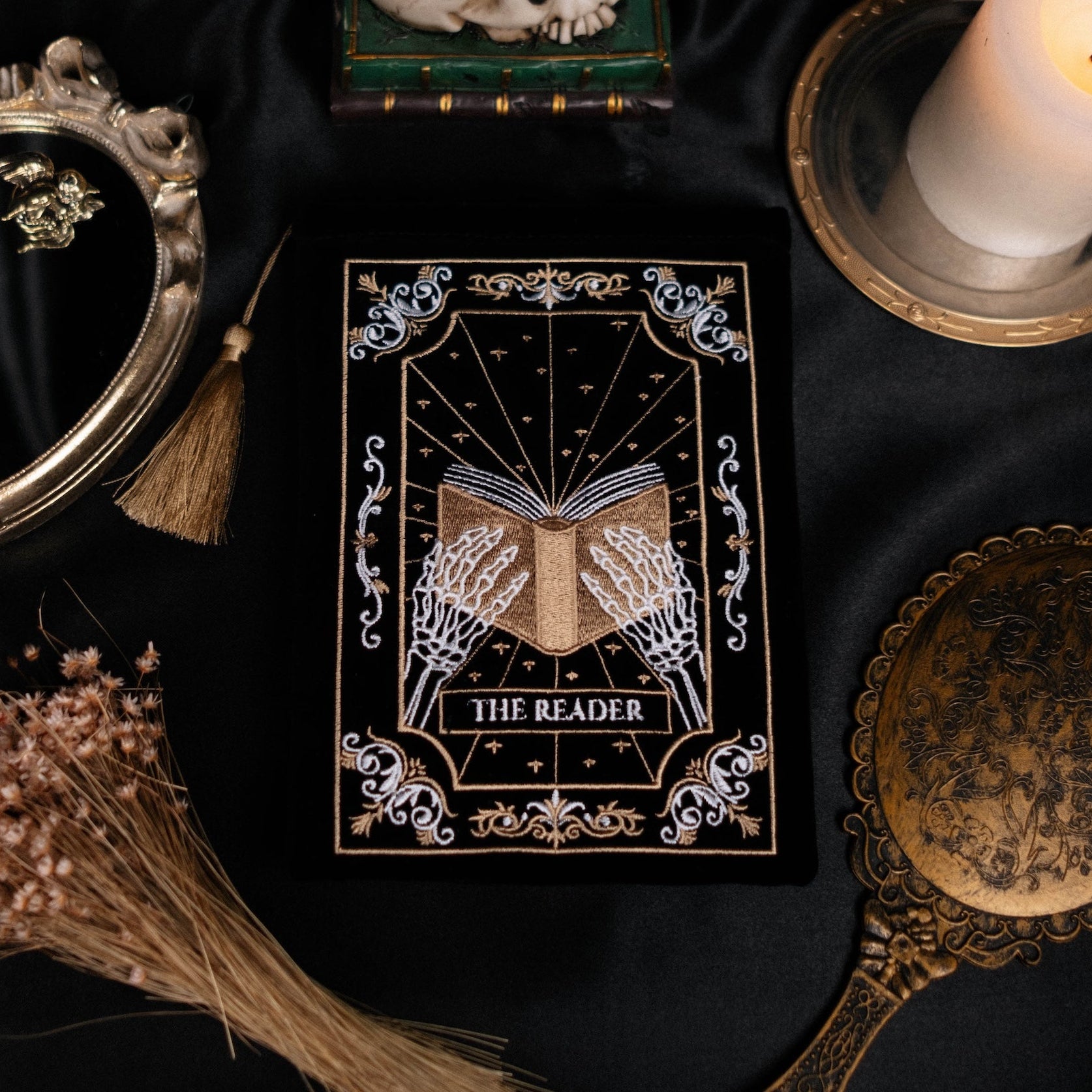 E-reader sleeve titled 'The Reader' with candles, mirror, and flowers on a dark fabric background