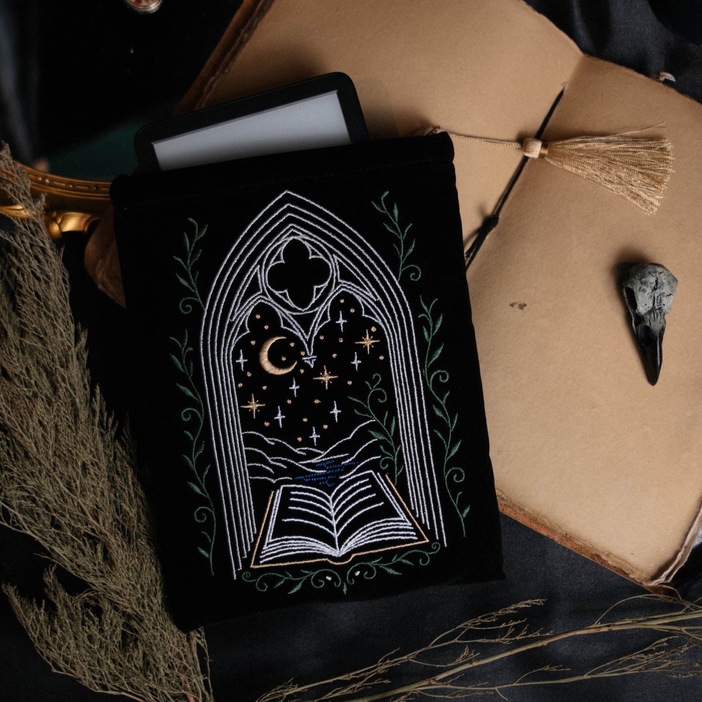 Decorative kindle pouch featuring a gothic window design surrounded by a beige book, on a dark fabric background.
